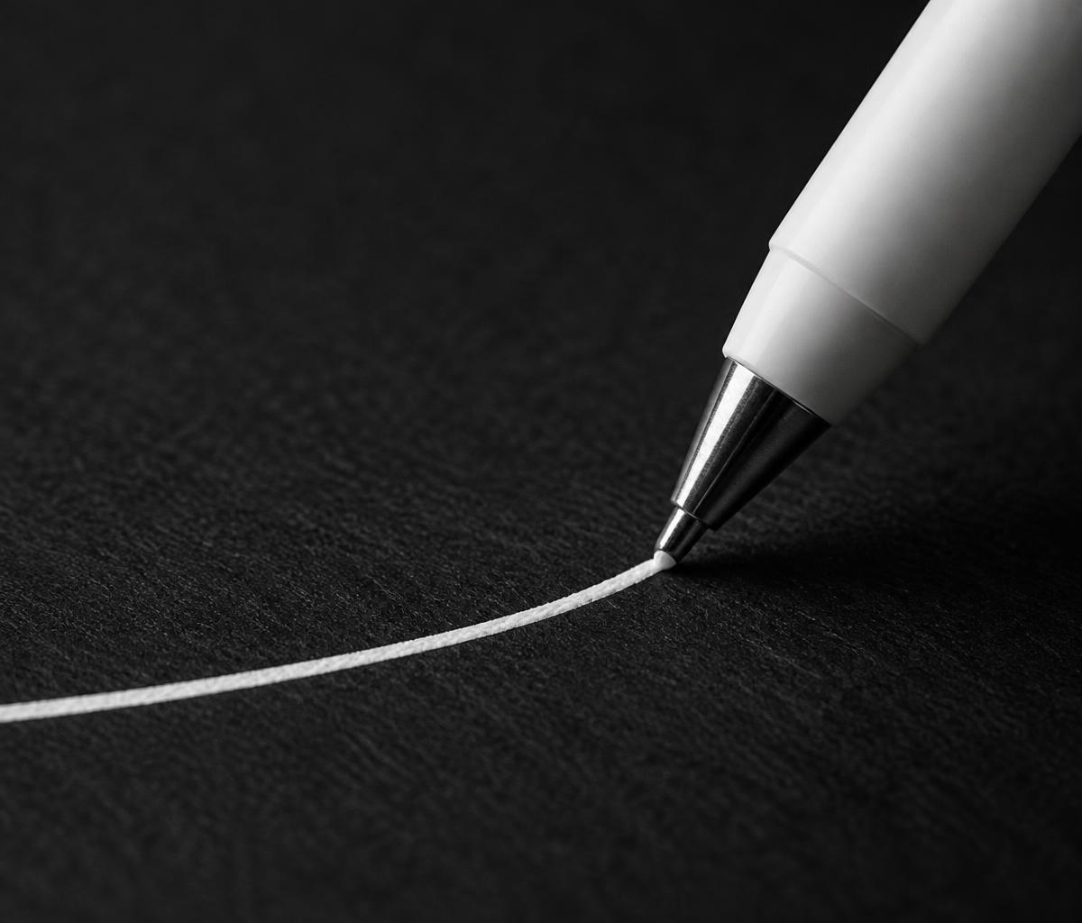 The tip of a white pen touching charcoal paper and leaving a crisp white line.